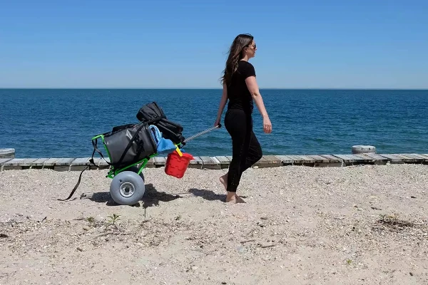 A woman pulling a WheelEEZ Beach Cart loaded with gear in the sand